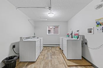 A room with two white refrigerators and a trash can.